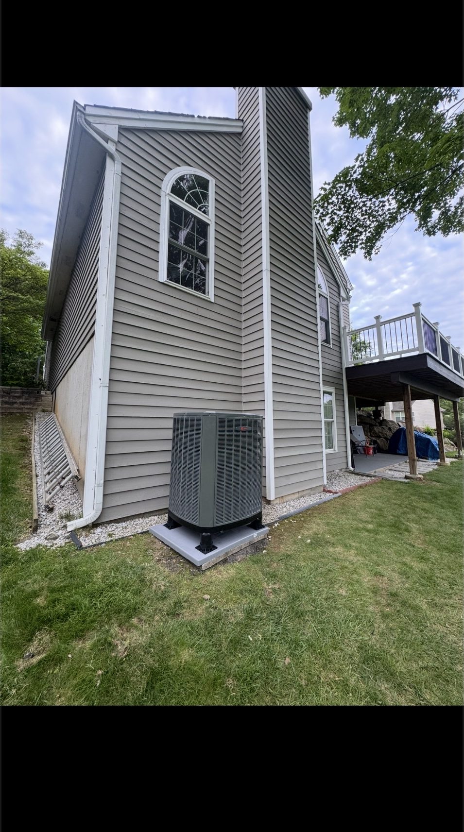 Outdoor AC condenser installed beside a two-story home with a deck